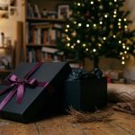 Black gift box with purple ribbon beside a Christmas tree