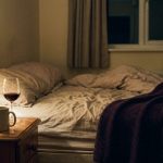 Lamplit bedroom with two glasses of red wine on the bedside table