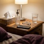 Bedside table with tissues, lubricant, phone and earbuds in a lamplit bedroom