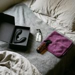 Unboxed prostate massager with lubricant, toy cleaner and towel laid out on a bed