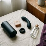 Male sex toys laid out on a bed: stroker, sleeve, cock ring, prostate massager and lubricant