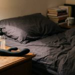 Curved black prostate massager on a bedside table beside lubricant and a purple towel